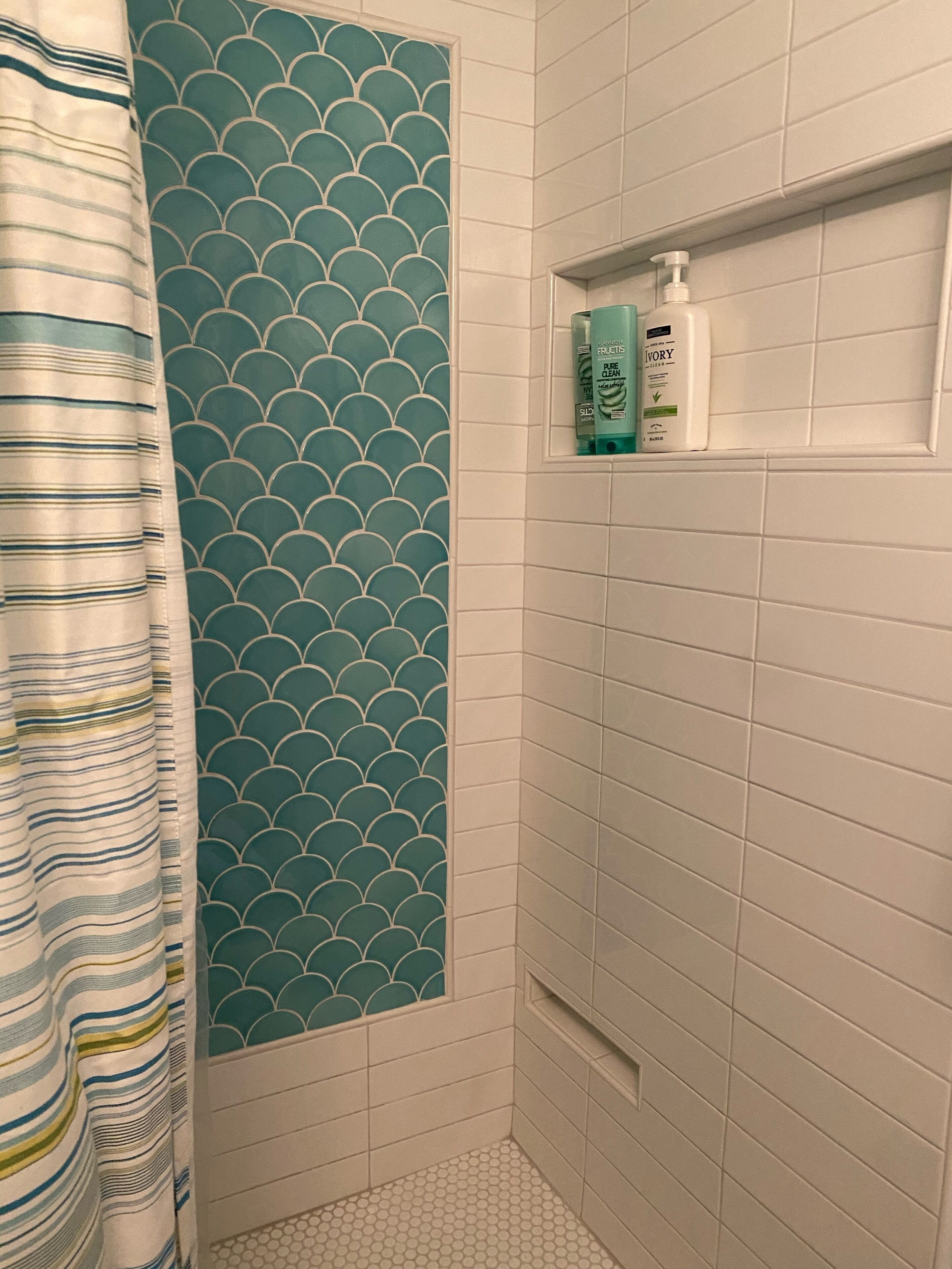 Une salle de bain avec un espace douche, un mur carrelé orné d’un motif bleu et une étagère contenant des articles de toilette.