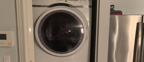A compact washer-dryer unit with a digital display, a stainless steel refrigerator, and a white door frame.