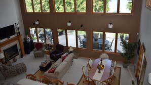 Un salon spacieux avec une grande table à manger, de nombreux espaces pour s’asseoir et une vue sur un lac grâce à de grandes fenêtres.