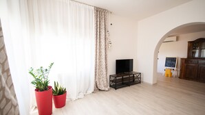 A living room with a large window, a flat-screen TV, a wooden coffee table, and two potted plants. - Il Cortiletto - Appartamento Lores (Manerba del Garda)