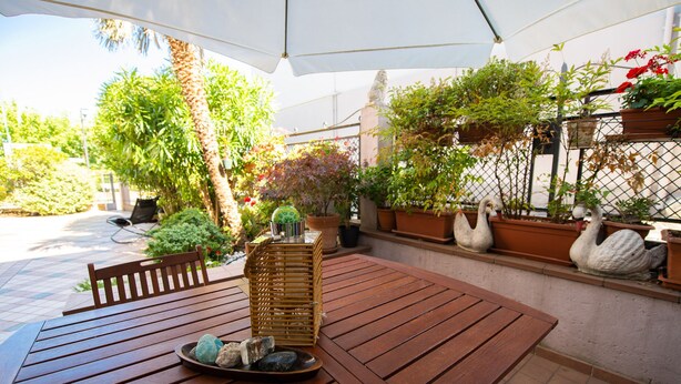 A wooden table with a woven basket and a plate of rocks, surrounded by potted plants and a white swan statue. - Il Cortiletto - Appartamento Lores (Manerba del Garda)