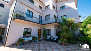 A multi-story building with a balcony, outdoor seating area, and potted plants. - Il Cortiletto - Appartamento Lores (Manerba del Garda)