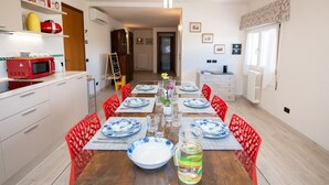 A dining area with a wooden table set for four, surrounded by red chairs. There are plates, glasses, and a pitcher on the table. - Il Cortiletto - Appartamento Lores (Manerba del Garda)