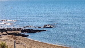 Ein Küstenstrand mit klarem, blauem Wasser, Felsen und einem Sandstrand.