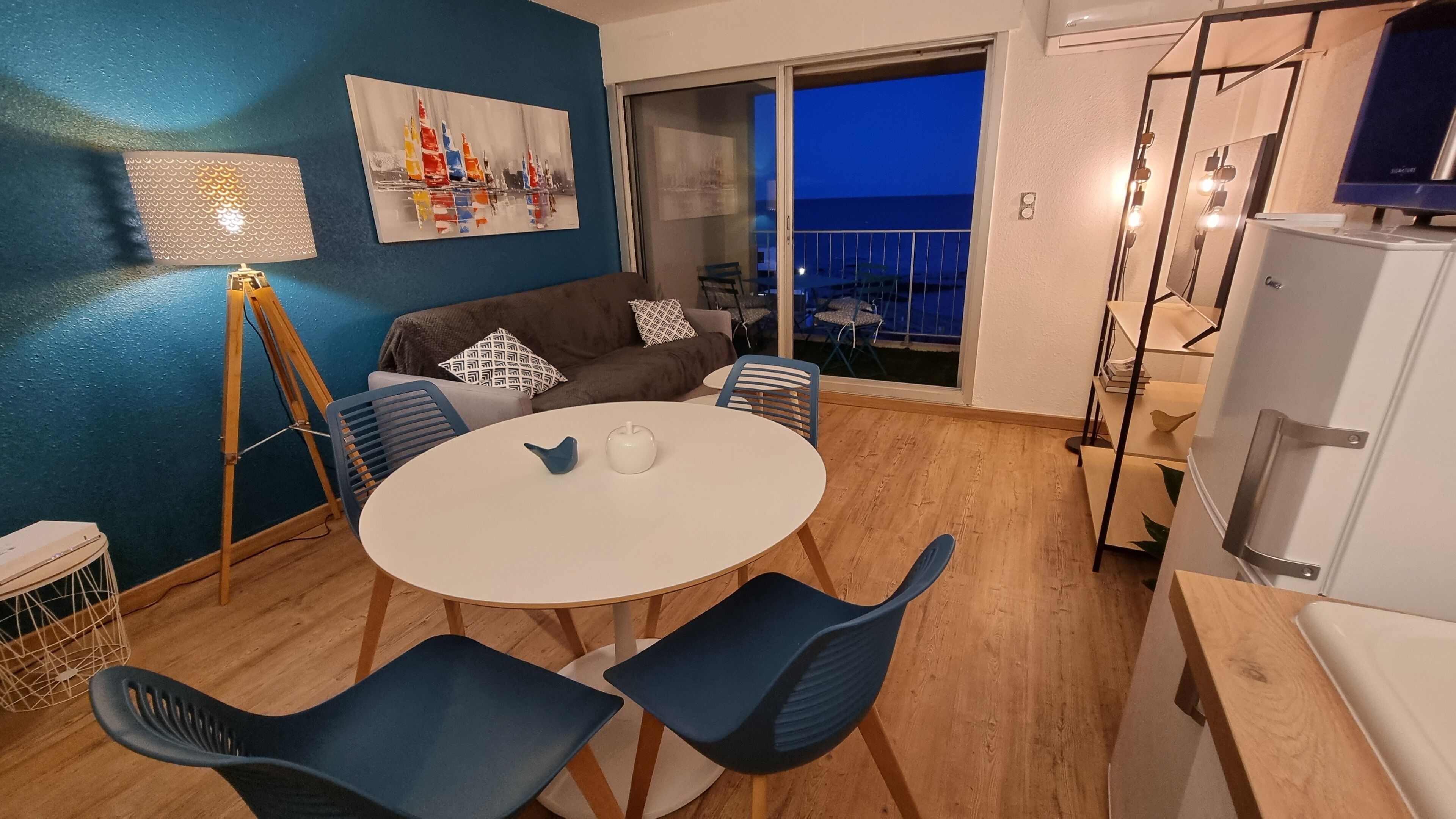 Ein gemütlicher Wohnbereich mit einem runden Tisch, blauen Stühlen, einer Couch und einem Gemälde an der Wand.