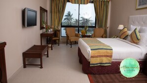 A hotel room with a bed, two armchairs, a desk with a chair, a TV, and a window with curtains. - Beach Luxury Hotel (Karachi)