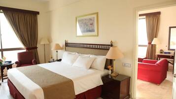 A hotel room with a large bed, two bedside tables with lamps, a chair, a red sofa, and a painting on the wall.