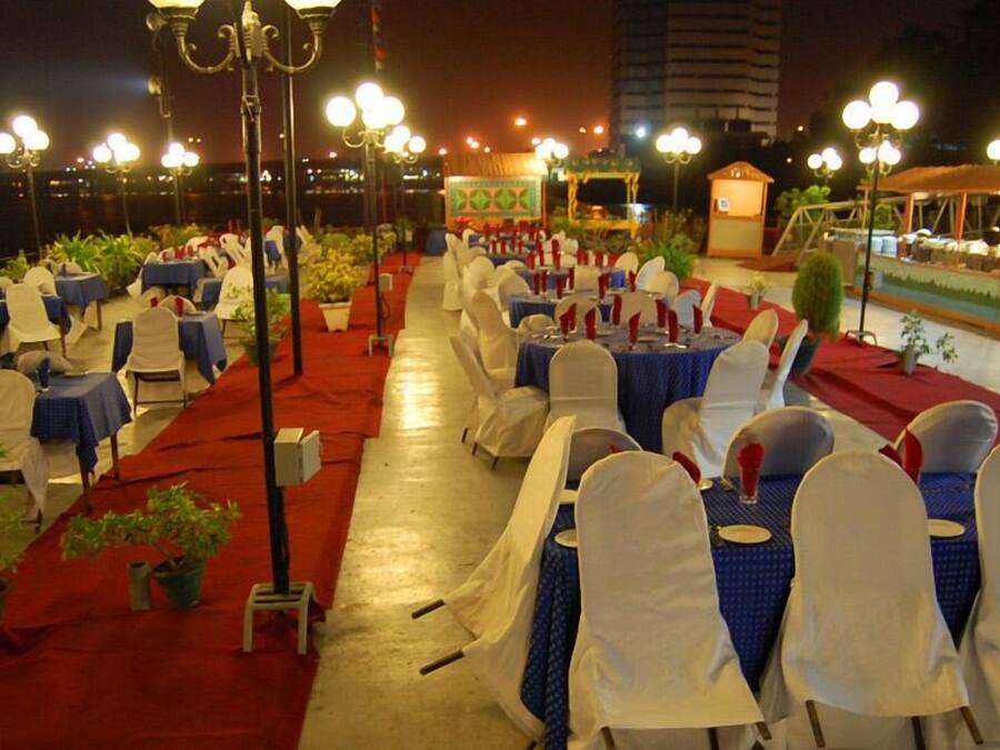 Une salle de réception en plein air, avec des rangées de tables et de chaises, un sol recouvert de moquette rouge et un éclairage décoratif.