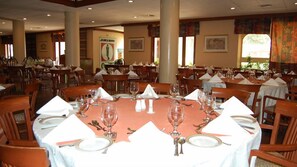 A dining area with round tables set for service, wooden chairs, and a large window with curtains. - Beach Luxury Hotel (Karachi)