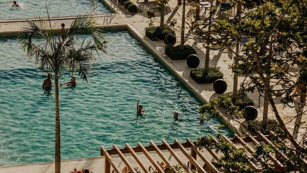 A swimming pool with people, surrounded by trees and outdoor seating.