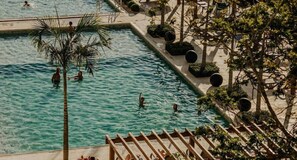 Ein Schwimmbad mit Personen, umgeben von Bäumen und Sitzgelegenheiten im Freien.