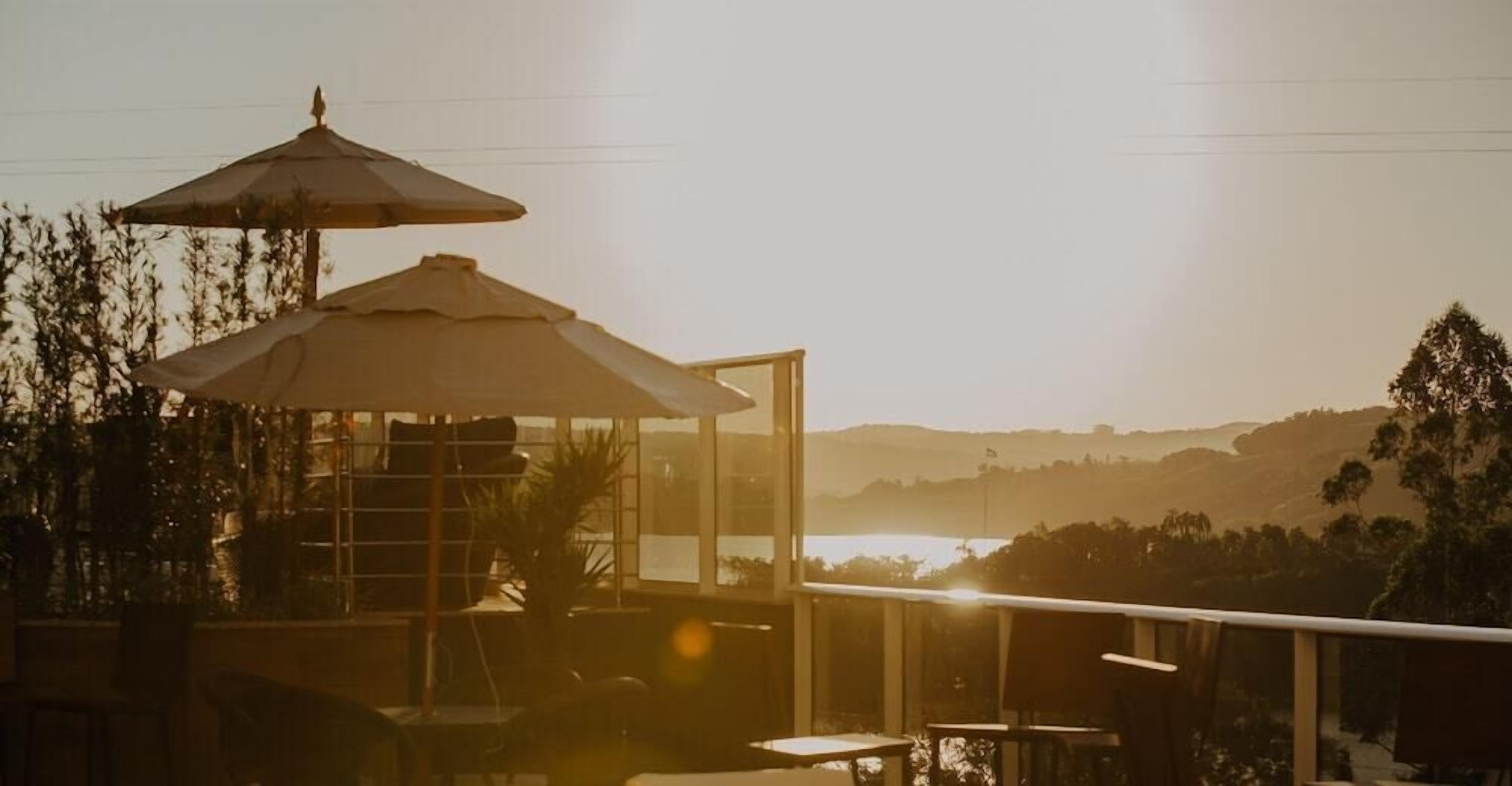 Um terraço com mesa e cadeiras, guarda-corpo de vidro e vista para a paisagem.