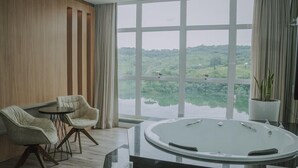 A modern bathroom with a large bathtub, two chairs, a small table, and a view of a lake.