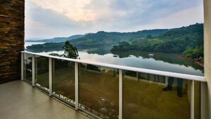 A balcony with a glass railing overlooking a lake and hills.