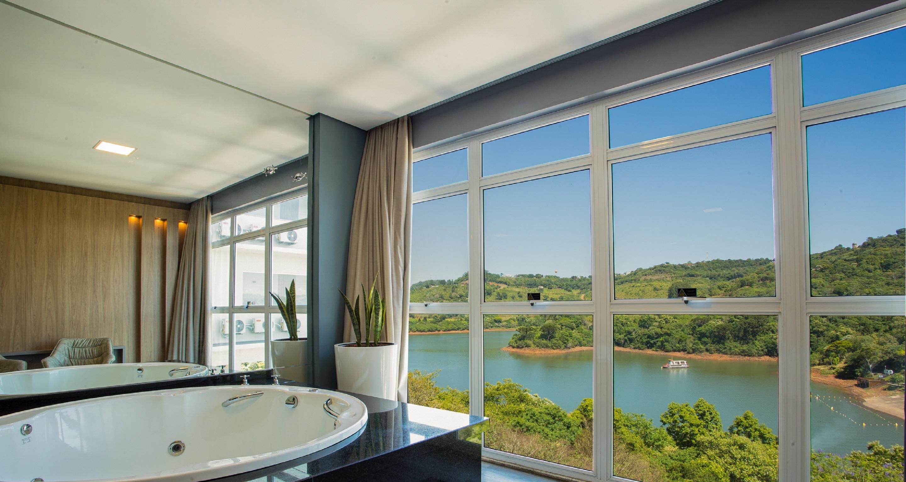 Um banheiro moderno com uma banheira grande, um espelho e vista para um lago com vegetação e um barco.