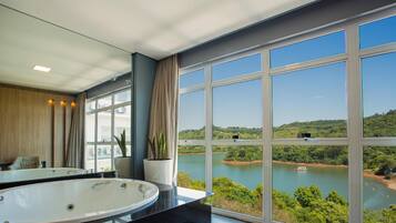 Um banheiro moderno com uma banheira grande, um espelho e vista para um lago com vegetação e um barco.