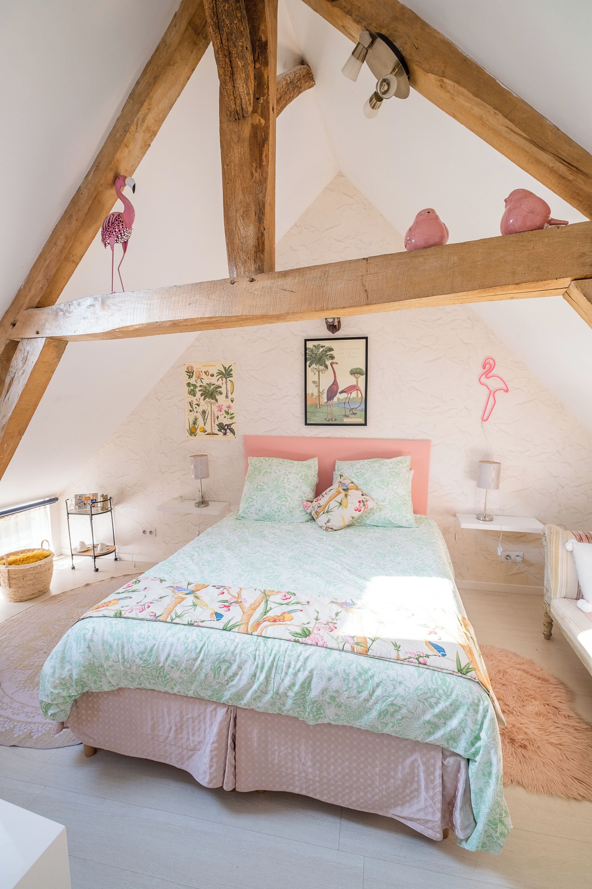 A bedroom with a sloped ceiling, a bed with floral bedding, a pink headboard, and a small side table.