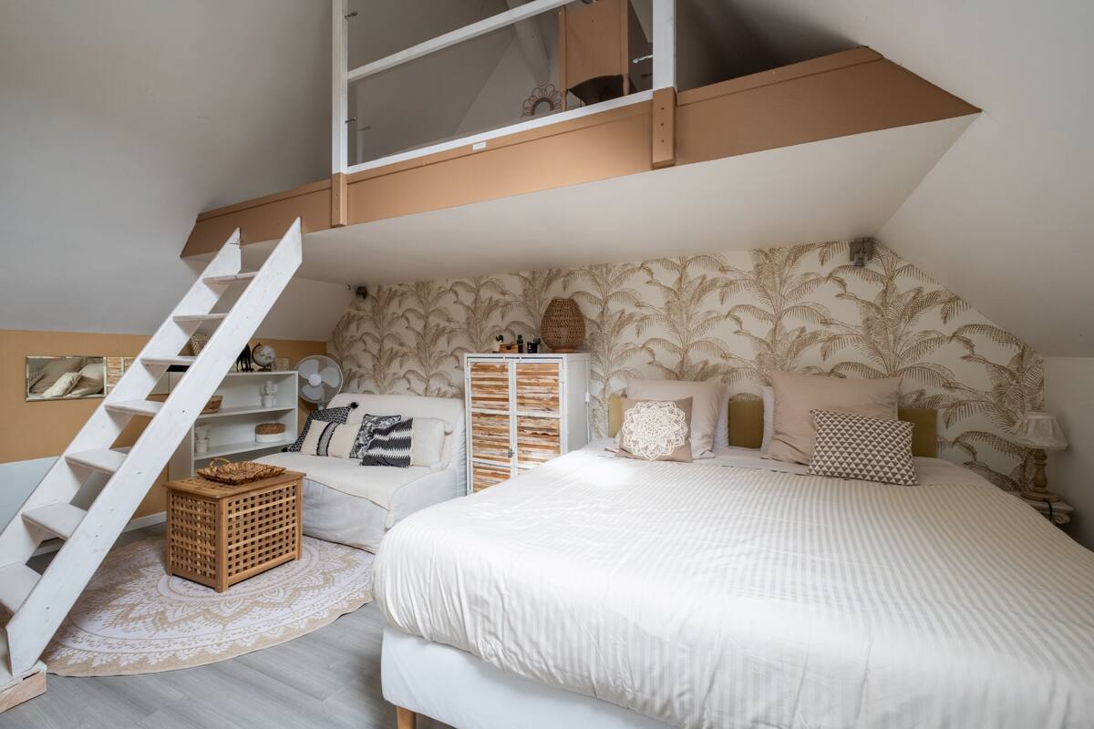 Un dormitorio con cama alta, una escalera, un aparador de madera y un papel tapiz estampado.