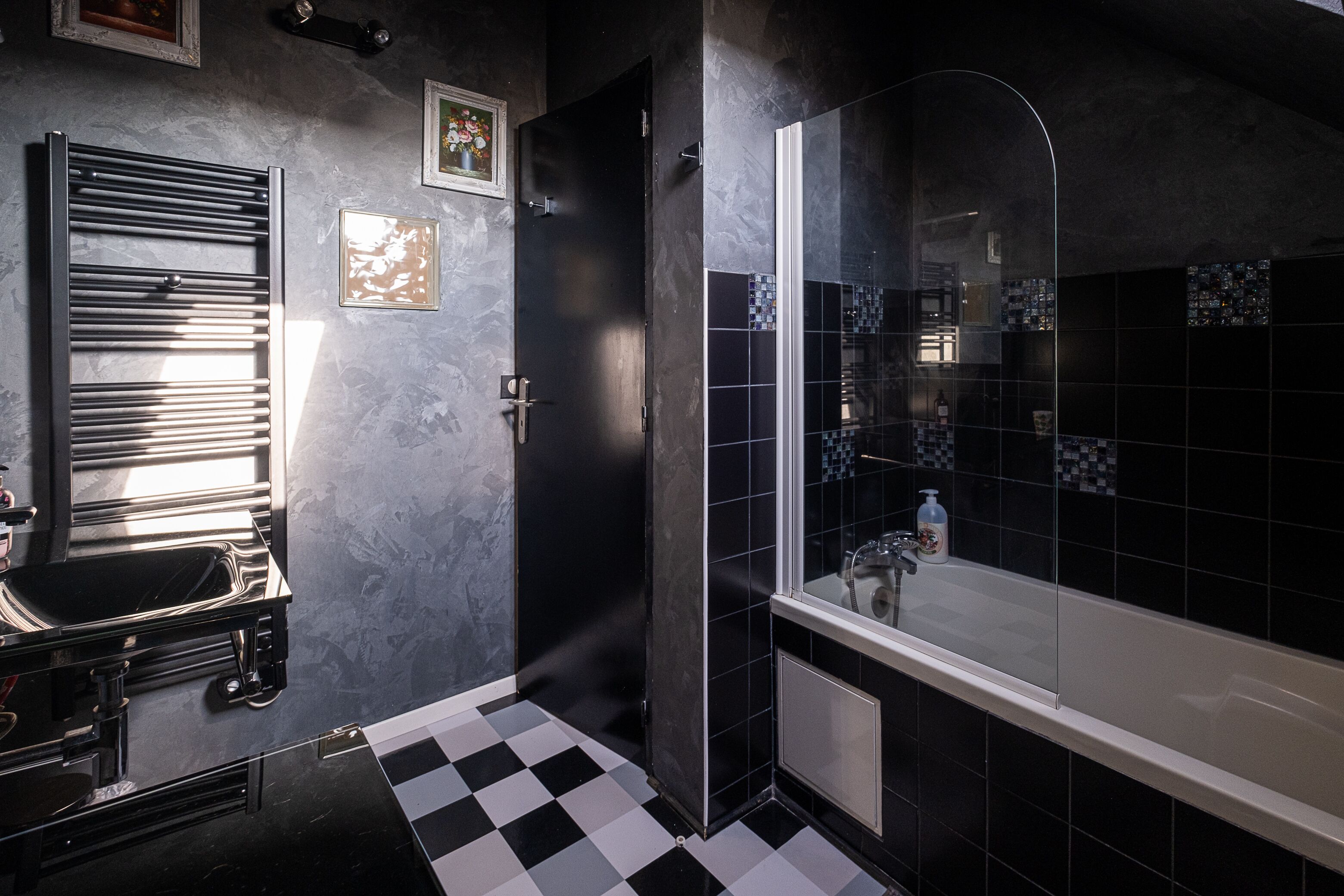Un baño moderno con piso a cuadros blanco y negro, ducha con cerramiento de vidrio y un espejo grande.