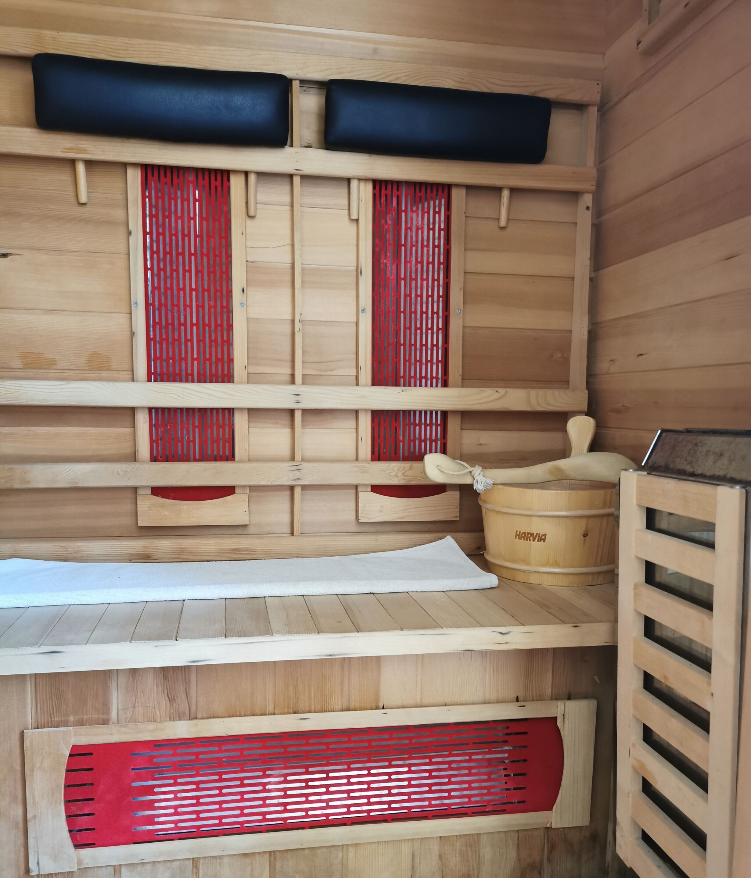A wooden sauna with a bench, a red and white perforated screen, and a Harvia sauna heater.