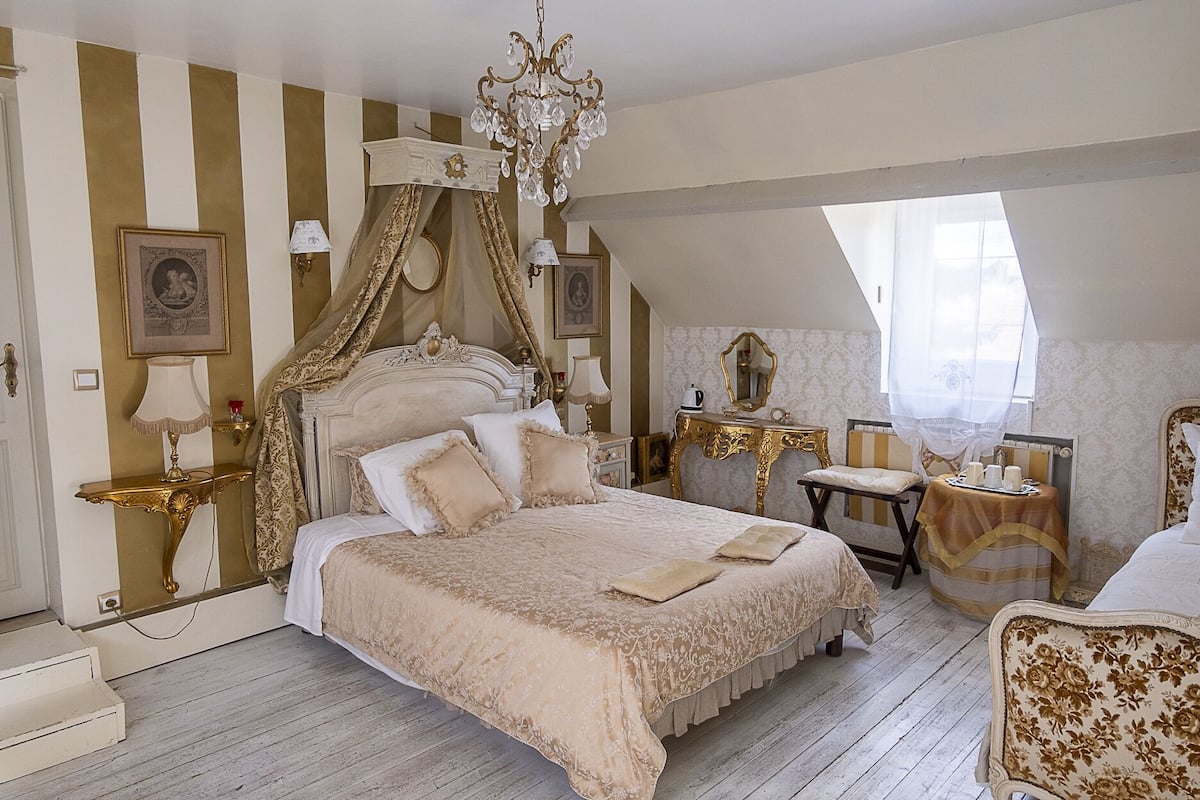 Une chambre à coucher avec un lit à baldaquin, un lustre, une coiffeuse avec un miroir et un fauteuil.