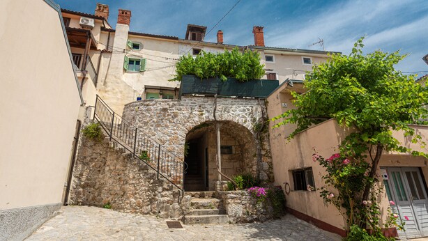 Un estrecho callejón con escalones de piedra que conducen a la entrada de un edificio, rodeado de vegetación y arquitectura tradicional.
