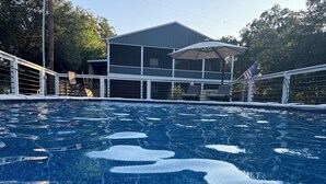 A swimming pool with a view of a house and trees in the background. - Downstairs Studio style apartment on the River (Mermentau)