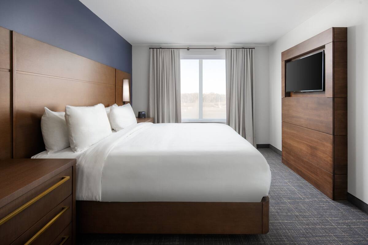 Ein Hotelzimmer mit einem großen Bett, einem Holz-Kopfbrett, einem Flachbildfernseher und Blick ins Freie durch ein großes Fenster.