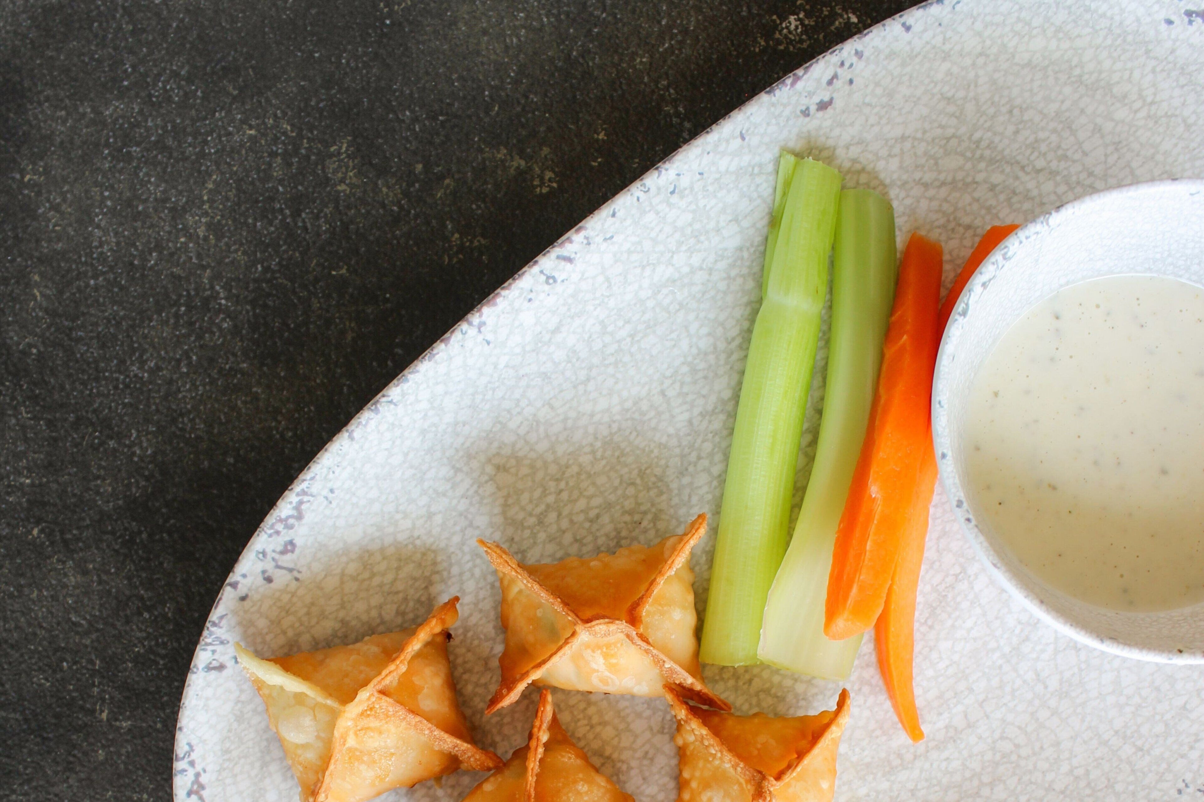 A plate with vegetable sticks, a small bowl of dip, and some fried snacks.