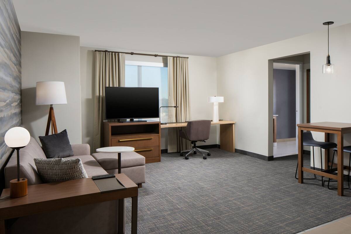 Ein Hotelzimmer mit Sofa, Schreibtisch, Fernseher und Esstisch.