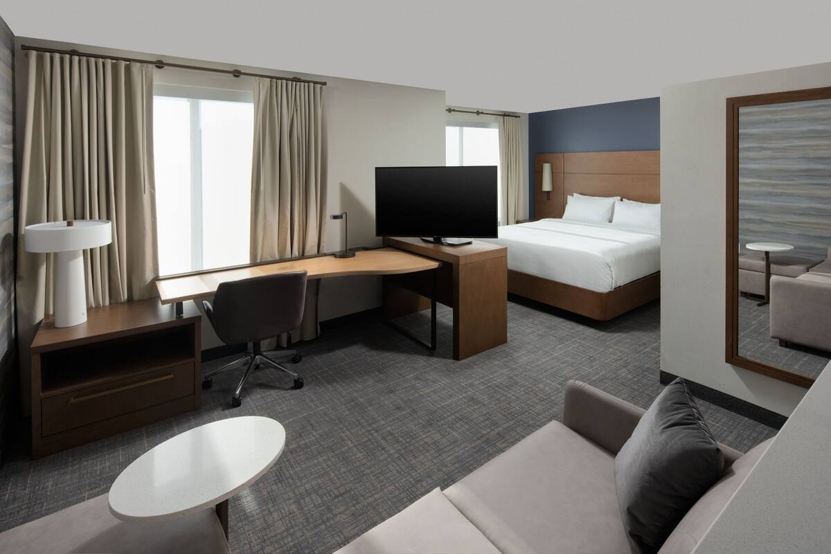 Ein Hotelzimmer mit Bett, Schreibtisch mit Computer, Fernseher, Sofa und kleinem Tisch.
