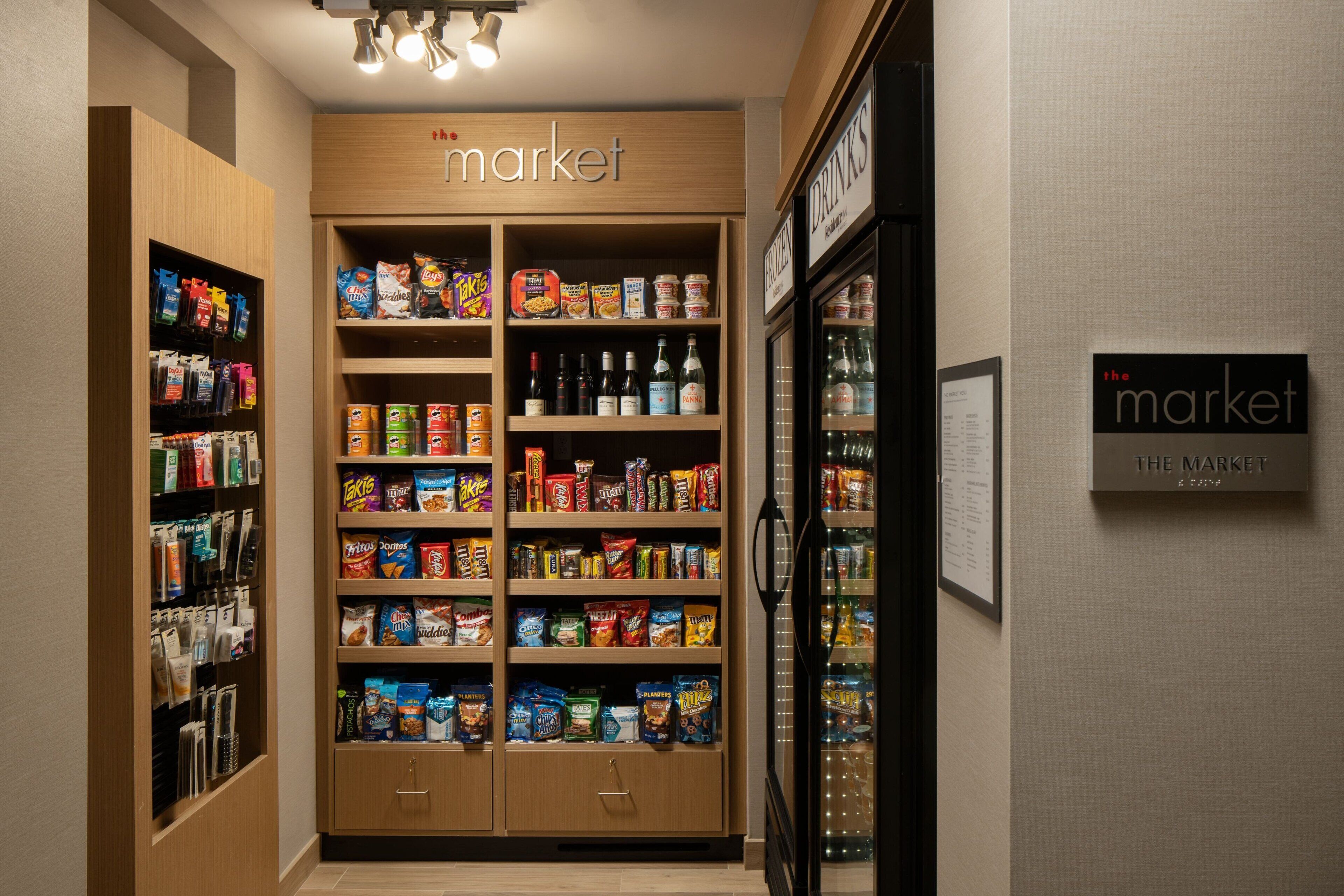 Un espace bien aménagé où l’on peut acheter des collations et des boissons dans un hôtel, avec plusieurs étagères remplies de divers produits.