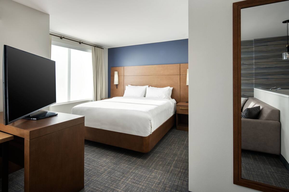 Ein Hotelzimmer mit einem großen Bett, einem Fernseher auf einem Holztischchen, einem Nachttisch und einem Spiegel.