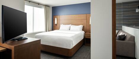 A hotel room with a large bed, a TV on a wooden desk, a nightstand, and a mirror.