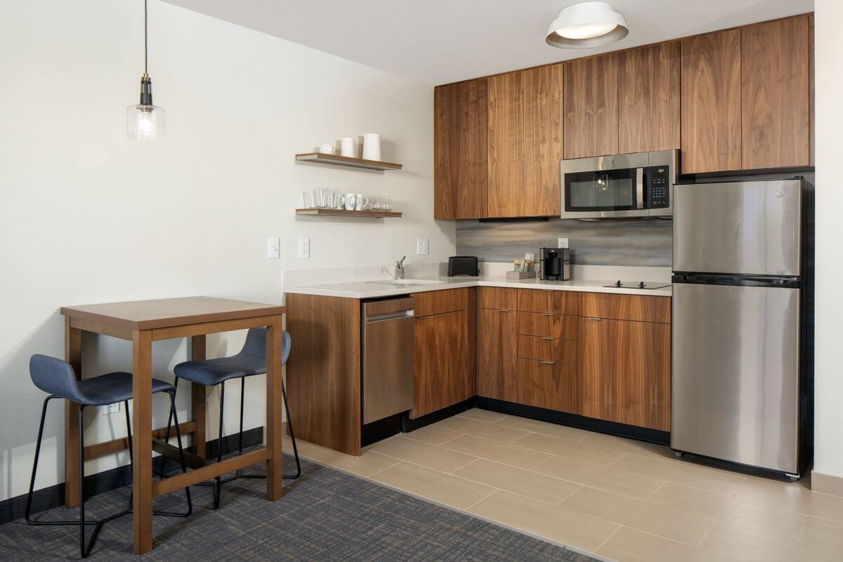 Eine moderne Küche mit Holzausbau, Edelstahlgeräten, einem Esstisch mit zwei Stühlen und einer Pendelleuchte.