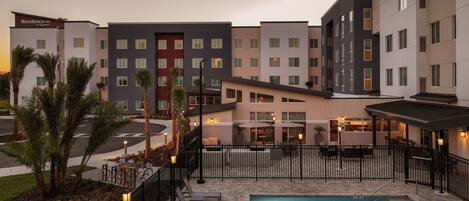 Un hotel con piscina, mobiliario exterior y vistas al atardecer.