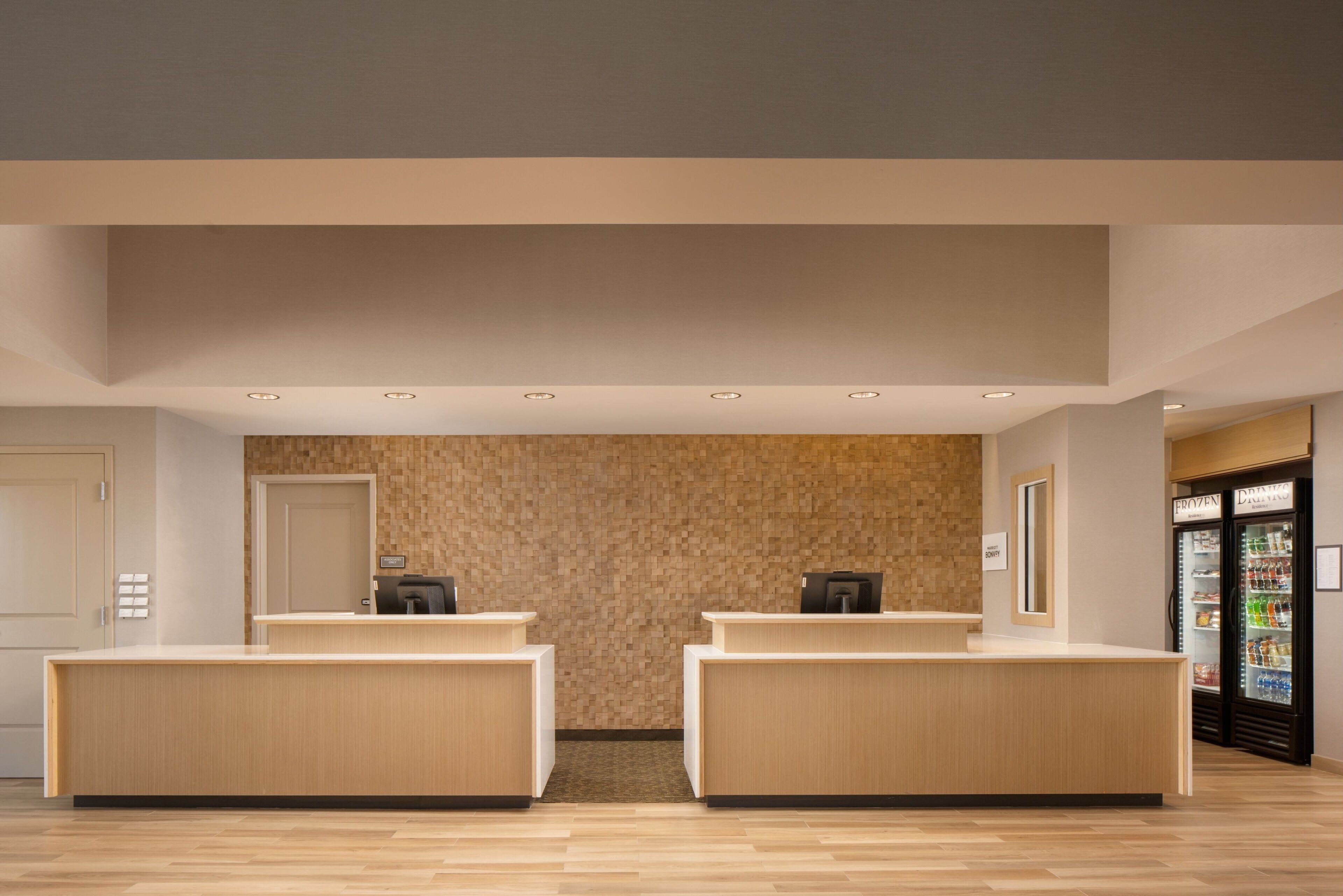 A reception area with two reception desks, a wall with a textured pattern, and a refrigerator stocked with beverages.