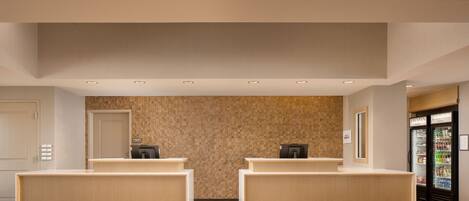 A reception area with two reception desks, a wall with a textured pattern, and a refrigerator stocked with beverages.