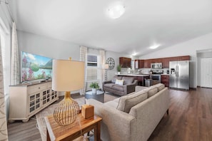 A modern living room with a sofa, a TV, a lamp, and a dining area with a kitchen in the background. - Private Home, Full Kitchen, Laundry & Wi-Fi! (Wasilla)