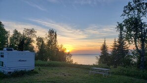 A camping area with a white RV, a picnic table, and a view of the sunset over a body of water. - Private Lake Superior Beachfront Retreat on 200 Acres (South Range)