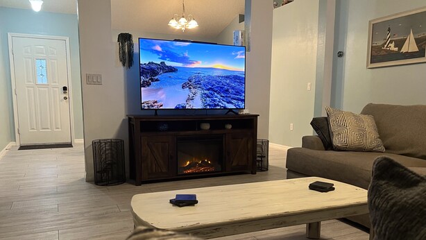 A living room with a flat-screen TV on a wooden stand, a fireplace, a sofa, and a coffee table.