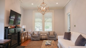 A living room with a fireplace, two armchairs, a white sofa, a coffee table, and a chandelier. - Beautifully Renovated in Heart of Cape May - 1 Block to Beach; 1 Block to Mall (Cape May)