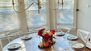 A round dining table with white chairs, a vase of flowers, and a chandelier. - Beautifully Renovated in Heart of Cape May - 1 Block to Beach; 1 Block to Mall (Cape May)