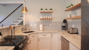 A modern kitchen with white cabinets, a black stove, a coffee maker, and a toaster. There are wooden shelves above the counter holding dishes and plants. - Beautifully Renovated in Heart of Cape May - 1 Block to Beach; 1 Block to Mall (Cape May)