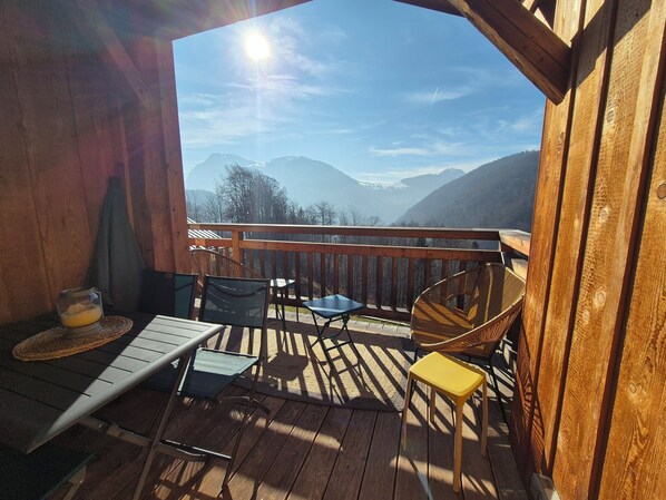 Enjoy a serene mountain view from this deck with a table, chairs, and wicker chair.