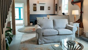 A cozy living room with a grey sofa, a glass coffee table, and a billiards set. There is a wooden ceiling and a window with a view. - Historic charm, all new amenities at Swallow's Rest: West (West Grove)