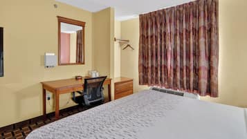 Habitación de hotel con cama, escritorio, silla, cómoda, espejo y ventana con cortinas.