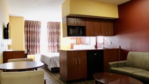 A compact hotel room with a kitchenette, a dining area, a sofa, and a bed. - HomeTown Inn & Suites (Longview)