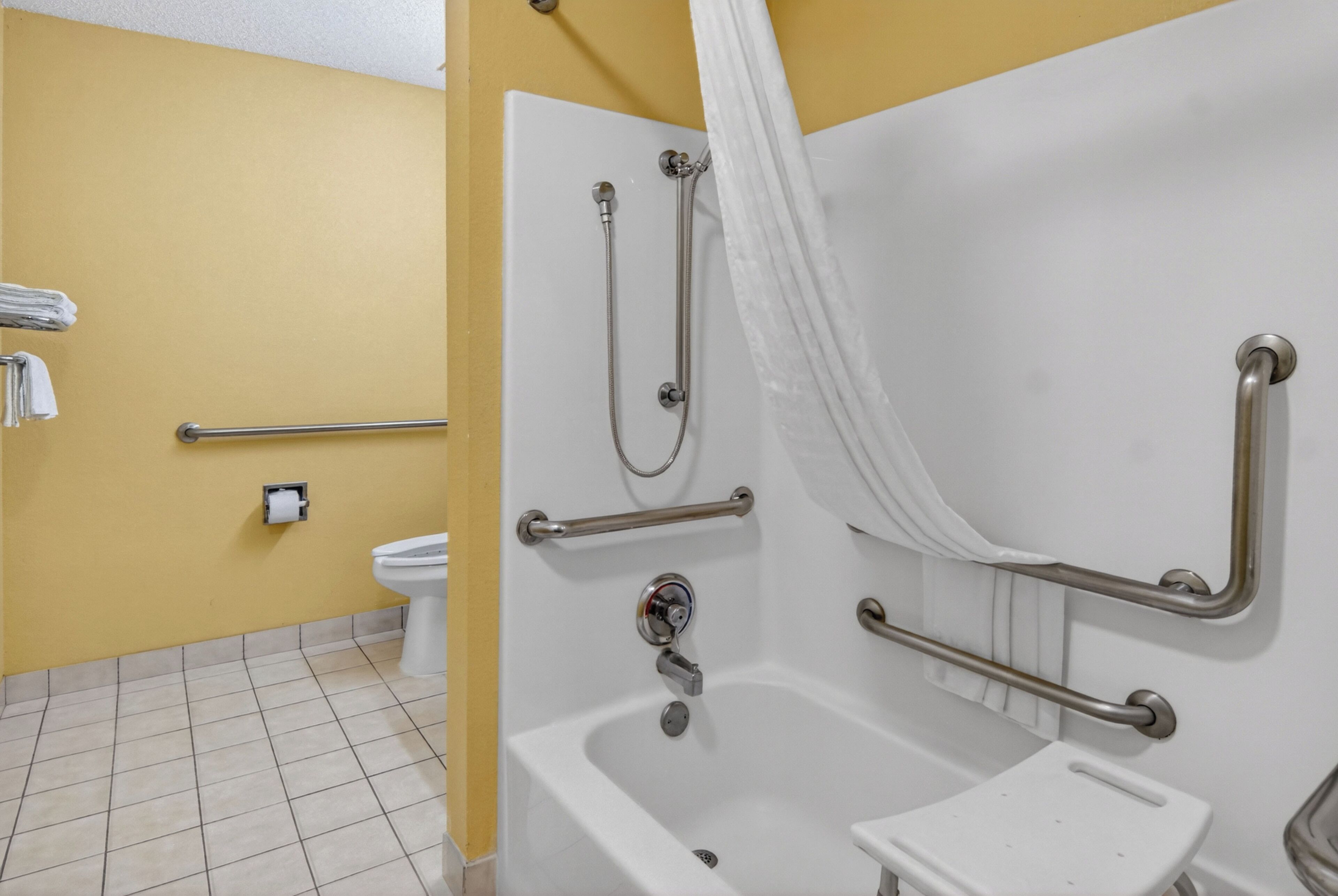 A bathroom with a white bathtub, grab bars, a toilet, and a towel rack.