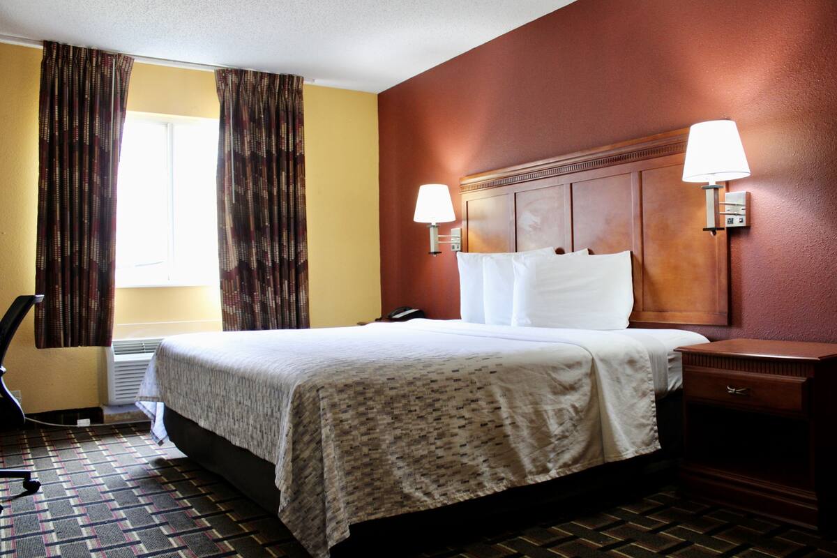 A hotel room with a bed, bedside lamps, a desk, and a chair.